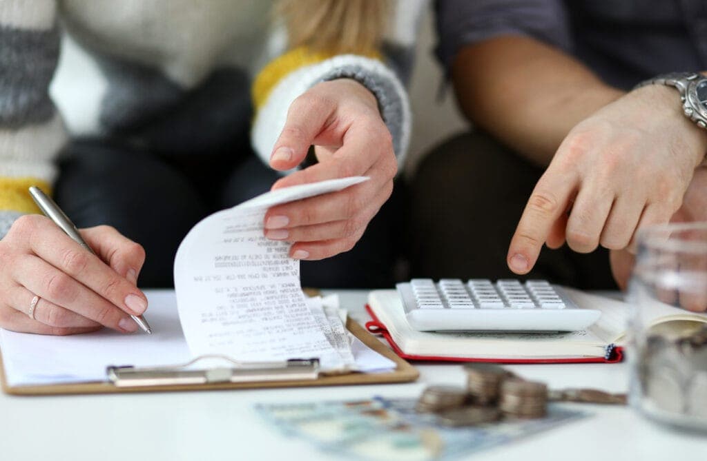 Two people doing financial planning at a table with a clipboard, calculator, and scattered currency.