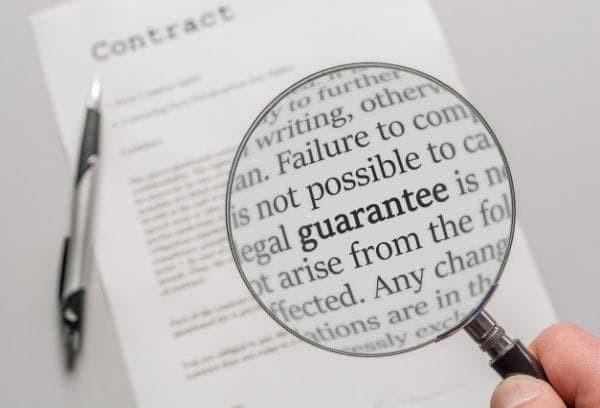 A magnifying glass enlarges text on a contract, highlighting the word "guarantee." A pen lies beside the document on a light surface, emphasizing important details.