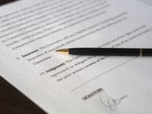 A black pen rests on a document with numbered sections titled "Insurance" and "Assignment." There's a signature near the bottom, indicating the document's potential legal or formal nature.