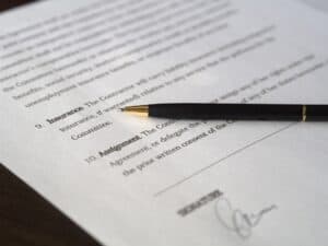 A black pen rests on a document with numbered sections titled "Insurance" and "Assignment." There's a signature near the bottom, indicating the document's potential legal or formal nature.