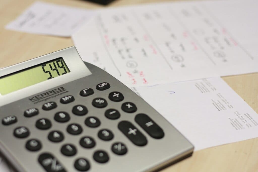 A calculator displaying "5.49" rests on a wooden surface with a few sheets of paper scattered around, suggesting a work or study environment.